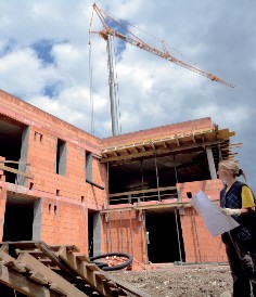 Photo of a new building, with a crane in the background and a woman holding construction plans in the foreground.