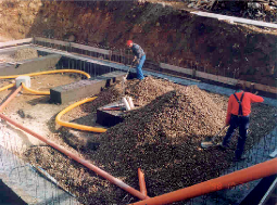 Photo of a radon drainage system installation. Two workers shovel gravel onto the pre-installed radon drainage system.